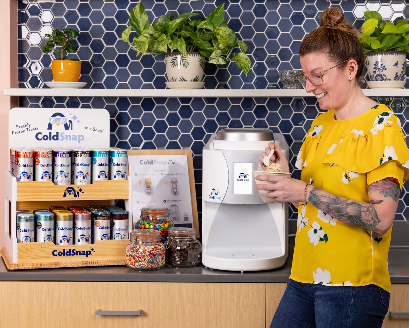 Woman in a yellow top enjoying a Coldsnap frozen treat, next to the ColdSnap machine and line of pods