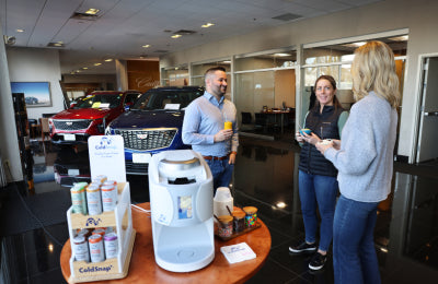 People interacting in a car dealership with a display of ColdSnap products.