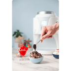 Person drizzling chocolate sauce over a bowl of ColdSnap® Chocolate Premium Ice Cream beside a bowl of maraschino cherries