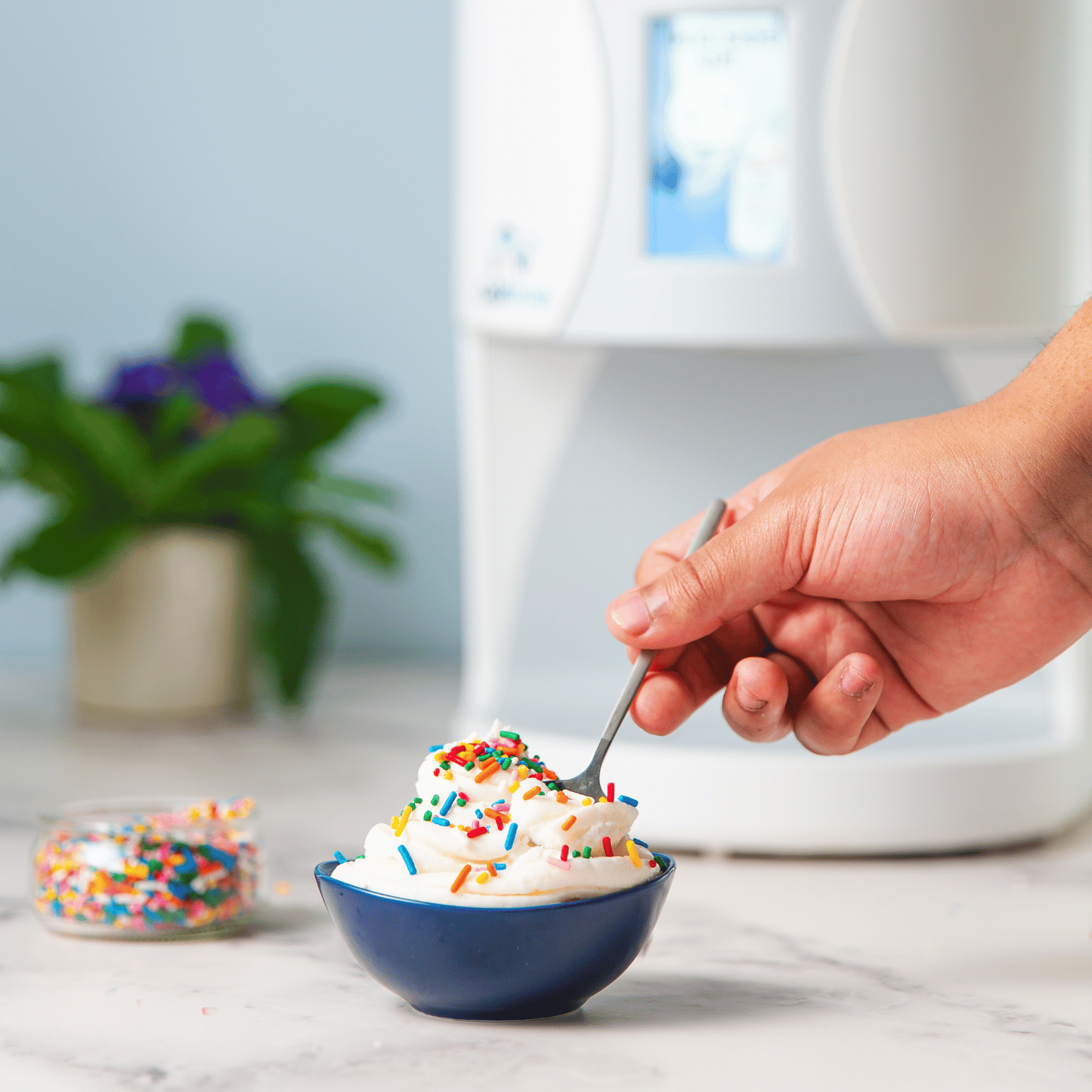 Hand using a spoon to scoop from a bowl of ColdSnap® ice cream with multicolored sprinkles. 