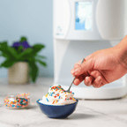 Hand using a spoon to scoop from a bowl of ColdSnap® ice cream with multicolored sprinkles. 