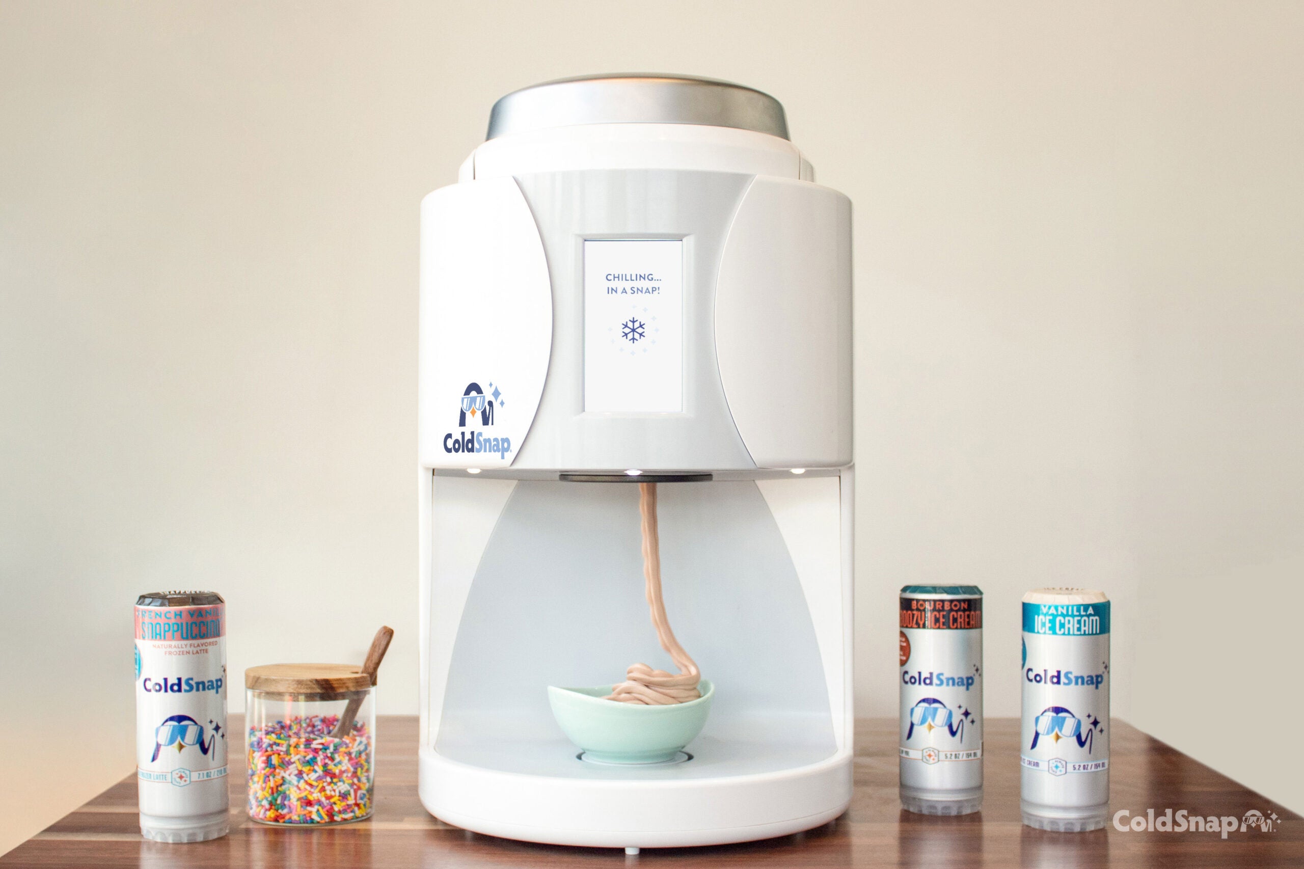 ColdSnap ice cream machine, surrounded by ColdSnap cans, dispensing ice cream into a bowl on a wooden surface