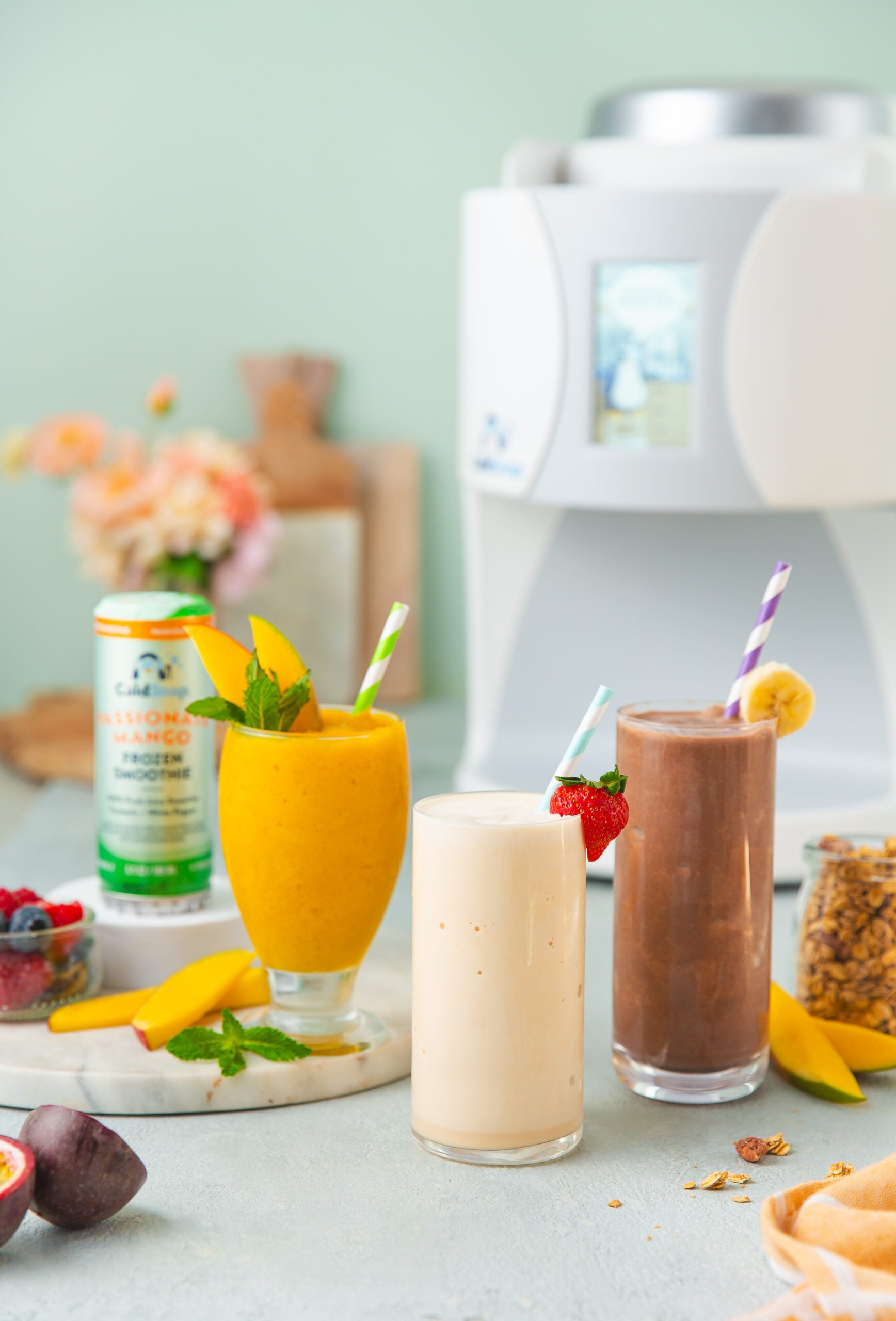 Three smoothie glasses with straws on a table with a kitchen background