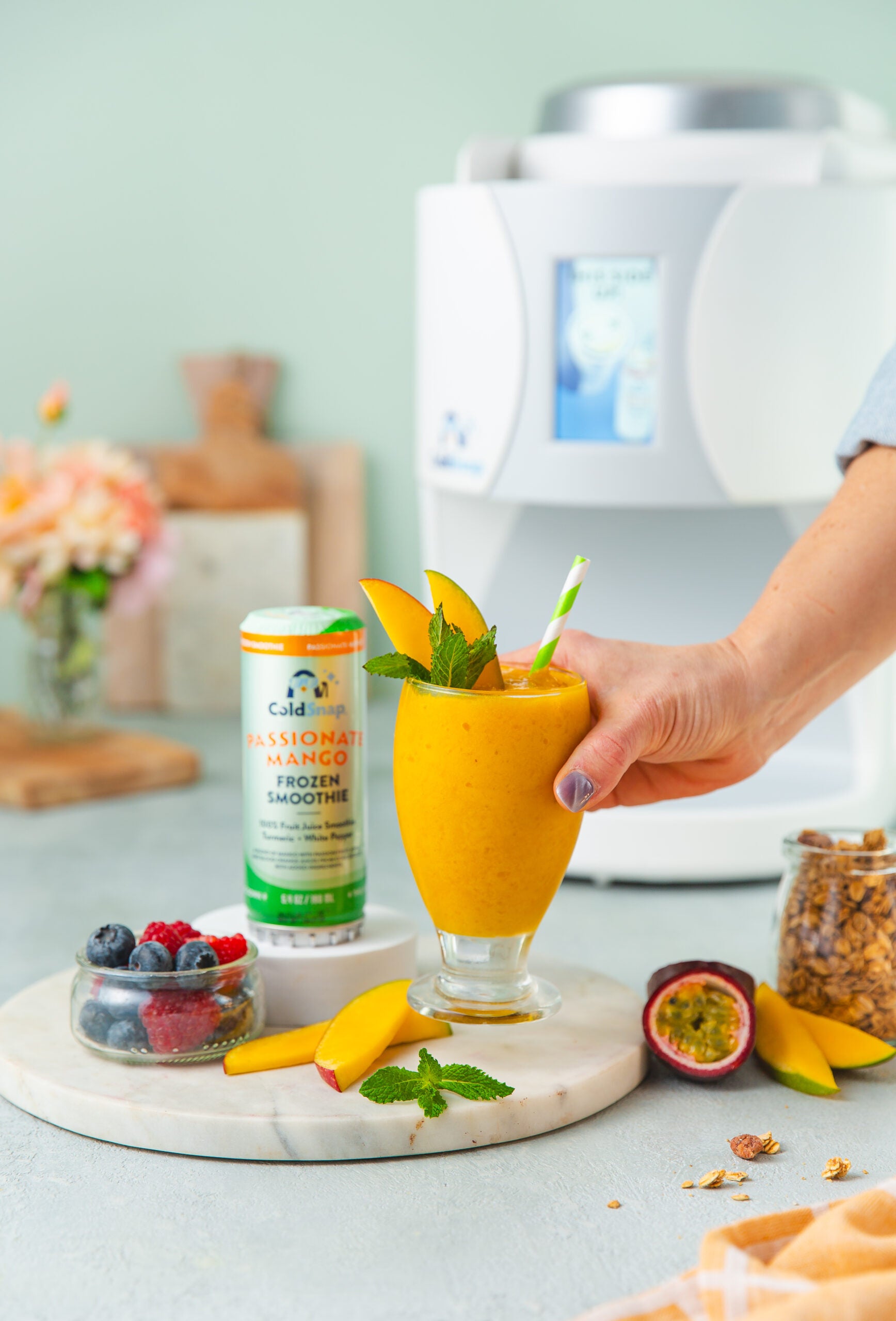 Person holding a Passionate Mango Frozen smoothie with a ColdSnap machine in the background. 