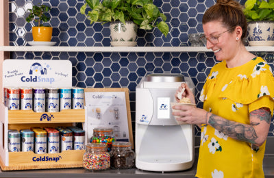 Person using a ColdSnap machine in a kitchen setting with shelves and decor.