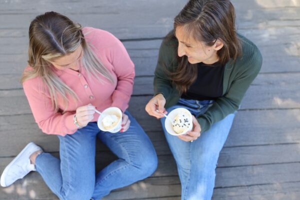 Two people sitting on a wooden deck eating ColdSnap ice cream.