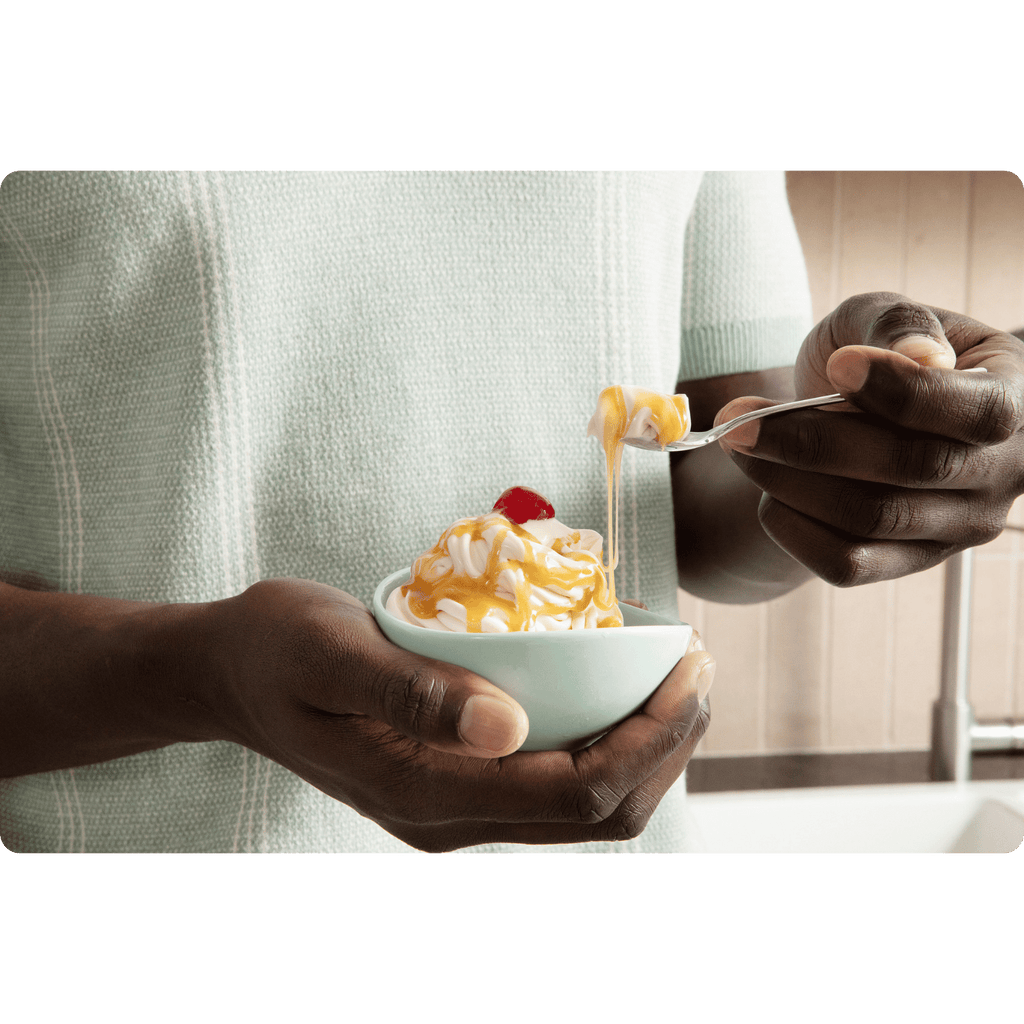 Person holding a bowl of prepared ColdSnap® Salted Caramel Premium Ice Cream topped with Salted Caramel and a cherry, bring a scoop to their mouth with a spoon