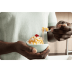 Person holding a bowl of prepared ColdSnap® Salted Caramel Premium Ice Cream topped with Salted Caramel and a cherry, bring a scoop to their mouth with a spoon