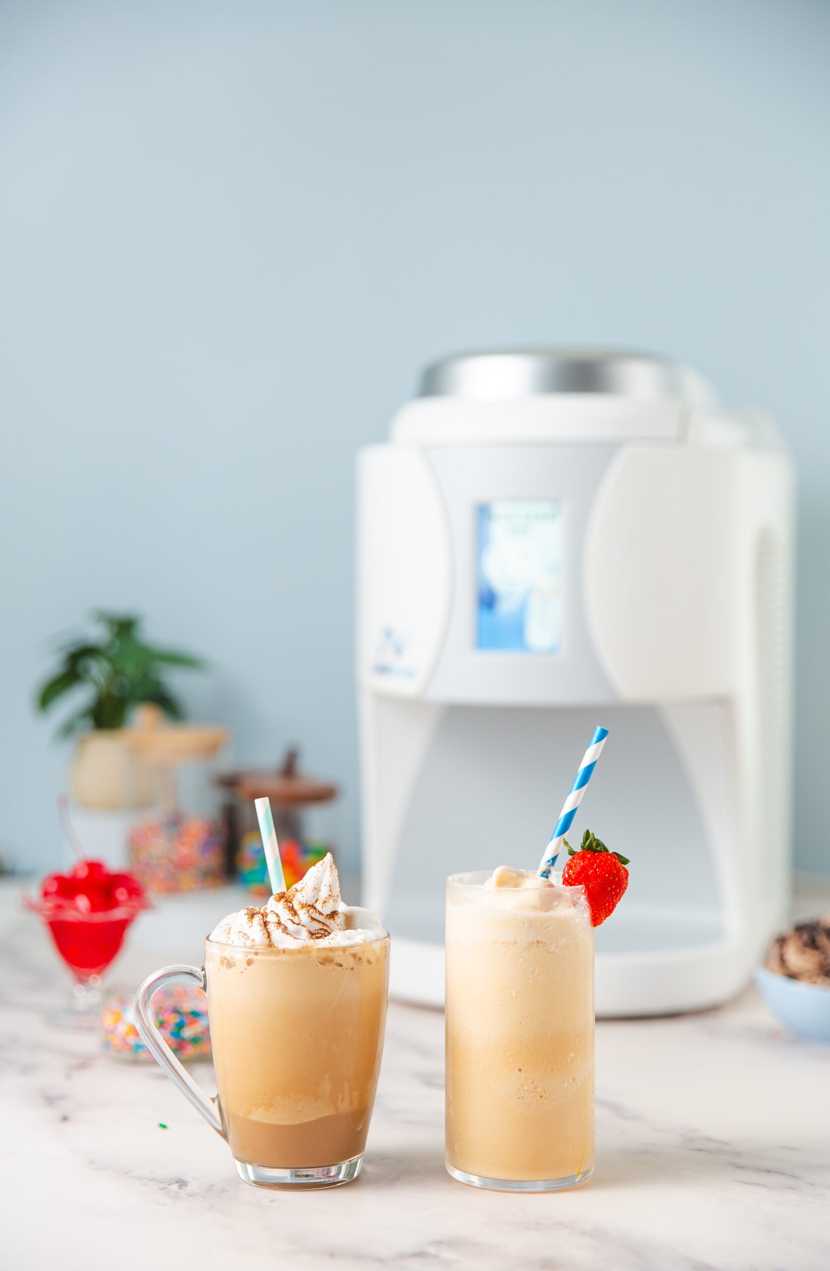 Two ColdSnap drinks with whipped cream and straws in front of a ColdSnap machine. 