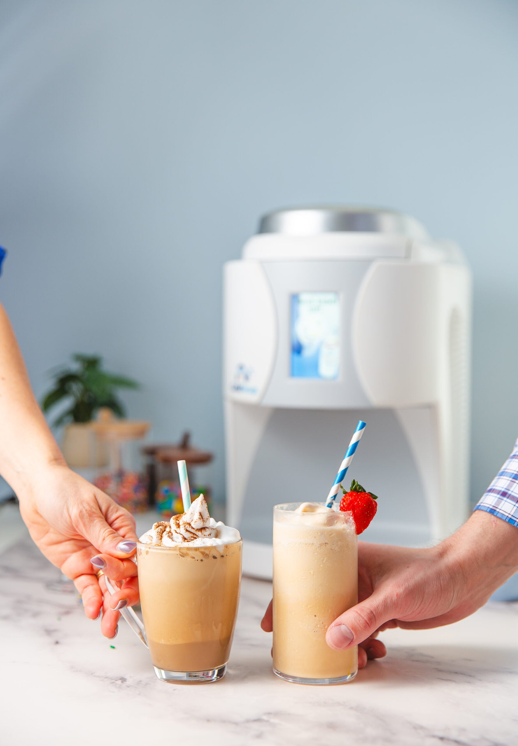 Two hands holding ColdSnap beverages with a ColdSnap machine in the background
