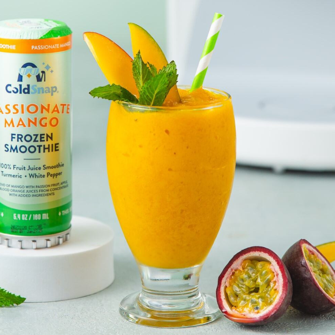 ColdSnap® Passionte Mango Smoothie Pod next to a prepared smoothie in a glass with a flared base, garnished with fresh mango, mint and straw, sitting on a countertop.
