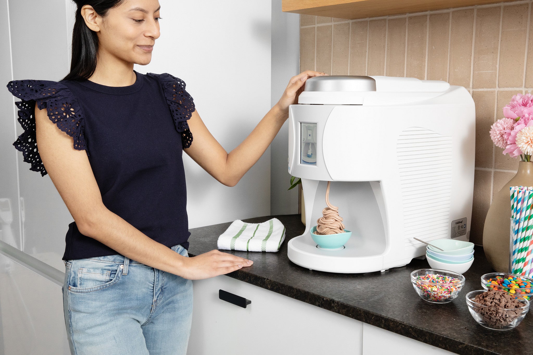 Woman using a ColdSnap machine on a countertop with various ice cream toppings around.