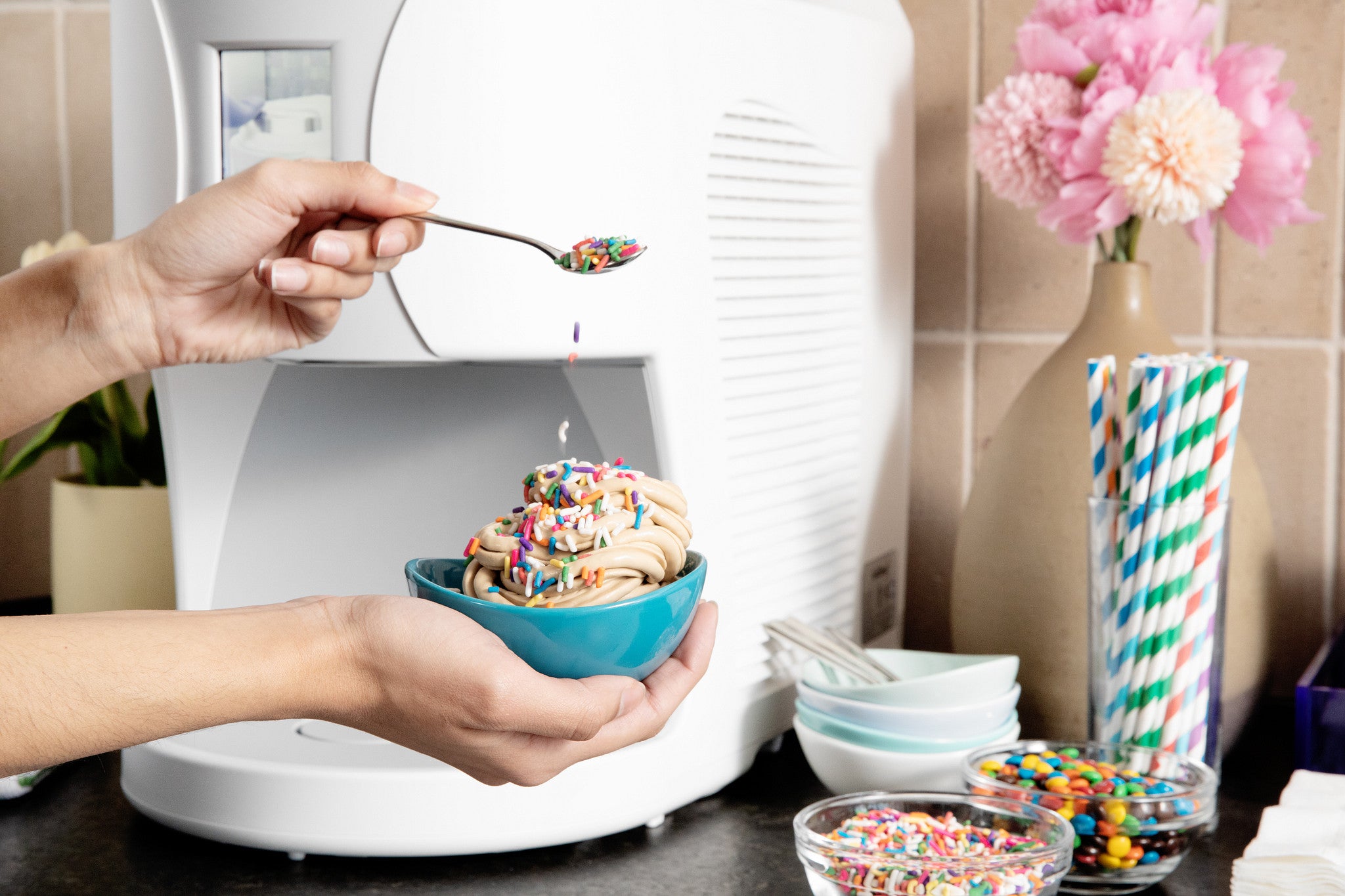 Person holding a bowl of ColdSnap ice cream with sprinkles in front of a ColdSnap machine.